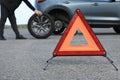 Man changing car tire near road, focus on emergency warning triangle Royalty Free Stock Photo
