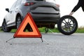 Man changing car tire near road, focus on emergency warning triangle Royalty Free Stock Photo