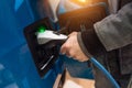 Man charging electro car at charging station. Man holding in hand power cable supply plugged in