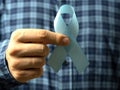 A man in a checked shirt holds a blue ribbon in his hand-a symbol of prostate cancer awareness. Close up, concept of medicine and