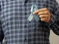 A man in a checked shirt holds a blue ribbon in his hand-a symbol of prostate cancer awareness.