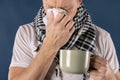 Man in a checkered scarf with big mug and tissue on blue background. Cold and flu illness relief Royalty Free Stock Photo