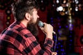 Man in checkered shirt holds microphone, singing song, karaoke club background. Guy likes to sing in dark karaoke hall Royalty Free Stock Photo