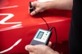 Man mechanic checking car paint thickness with electronic meter