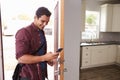 Man Checking Mobile Phone As He Opens Door Of Apartment