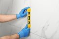 Man checking proper ceramic tile installation with level on wall. Building and renovation works Royalty Free Stock Photo