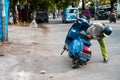 a man checks the engine of his red and blue vespa which broke down on the side of the road