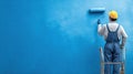 Man Checks Quality of Freshly Painted Wall in Work Site While Using Roller and Standing on Scaffold in Bright Blue Color Royalty Free Stock Photo