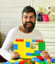 Man with cheerful face makes brick constructions for kids