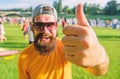 Man cheerful face shows thumb up. Man bearded in front of crowd riverside background. Top list summer festival must