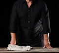 Man chef in a black shirt and apron stands near a wooden table, rested his hands Royalty Free Stock Photo