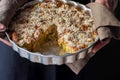 Man Chef Holding Baking Form with Homemade Vegan Eggless Apple Cake with Crumbles. Cut out Slice. Natural Light Cozy Atmosphere