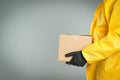 Man in chemical protective suit holding cardboard box on grey background, closeup view with space for text. Prevention of Royalty Free Stock Photo