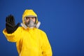 Man in chemical protective suit making stop gesture on blue background. Virus research