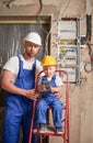 Man and child electricians posing near electrical panel in apartment.