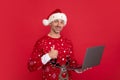 Man in Christmas sweater and hat work on laptop pc computer on color background. Middle aged santa. Royalty Free Stock Photo