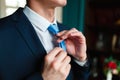 Man in a classic suit straightens his blue tie. Handsome elegant young fashion man in coat tuxedo classical costume suit and bow t Royalty Free Stock Photo