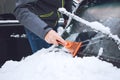 Man cleaning car from snow and ice with brush and scraper tool during snowfall. Winter emergency. Weather-related vehicle