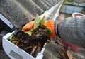 A man is cleaning a clogged roof gutter from dirt, debris and fallen leaves to prevent water damage and let rainwater drain