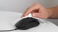 Man cleaning computer mouse with disinfecting wipe at white table indoors, closeup. Protective measures Royalty Free Stock Photo