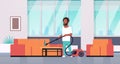 Man cleaning couch with vacuum cleaner african american guy doing housework concept modern living room interior male Royalty Free Stock Photo