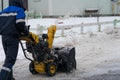 Man is cleaning the snow by the snowplow on a small street in a cottage village