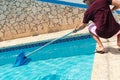Man cleaning swimming pool of fallen leaves with net in summer