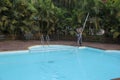 Man cleaning swimming pool with long pole