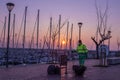 Man is cleaning up the city in the morning near a marina filled with several sailboats