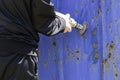 A man cleans old paint from an iron gate with a brush and an electric drill