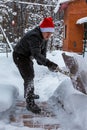 A man cleans steps from snow. In a red hat of Santa Claus and a leather black jacket. In felt boots. Clearing snow from the backya