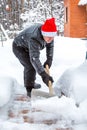 A man cleans steps from snow. In a red hat of Santa Claus and a leather black jacket. In felt boots. Clearing snow from the backya