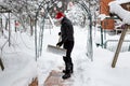 A man cleans steps from snow. In a red hat of Santa Claus and a leather black jacket. In felt boots. Clearing snow from the backya