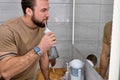 Pleased man cleans teeth using electric oral irrigator with jet of water, looking at mirror. Royalty Free Stock Photo