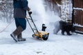 Man clears snow with a snow blower in house yard.