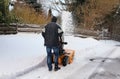 A man clears snow from the road in winter with a snow blower