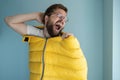 Man climbed into a yellow sleeping bag while standing indoors against a wall, imagining himself a tourist, yawns and Royalty Free Stock Photo