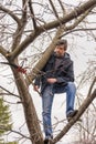 Man climbing high on an apple tree with pruner against sky. Pruning of fruit trees with lopper. Spring or autumn work in garden.