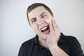 A man clings to his cheek and winces in pain in his tooth. The concept of dental problems, caries, tooth decay, flux. White