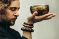 A man with closed eyes listens to the singing bowls. A man holds singing bowls in front of him. The rosary on hand.