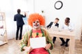 A man in a clown suit and a wig is sitting in the business office on April 1. Royalty Free Stock Photo