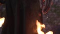 Man in the coat with a hood on his head standing in the fire. Burning of the warlock. Camera moving down