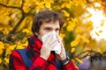 Man with cold rhinitis on autumn background. Fall flu season. Il