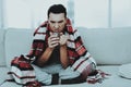 Man with Cold Sitting on Sofa in Checkered Blanket