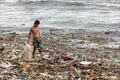 A man collecting plastic waste in a pile of garbage in the sea