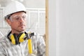 Man construction worker with the hammer nails the plank to the wall wear gloves, hard hat, glasses and hearing protection Royalty Free Stock Photo