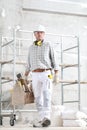 Man construction worker holding tool box wear gloves, hard hat, glasses and hearing protection headphones, at interior building Royalty Free Stock Photo