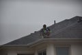 A man contractor worker on roof top working on a cloudy rainy day.standing sitting walking kneeling. fixing roof.rain water system