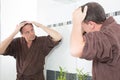 Man controls hair loss in the bathroom looking in a mirror Royalty Free Stock Photo