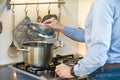 Man cooking in the kitchen while lifting the lid of a pot on the stove while the fire is lit. The man is wearing a light blue Royalty Free Stock Photo